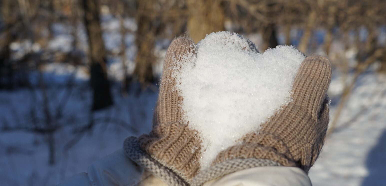 hands in brown mittens holding snow in a heart shape