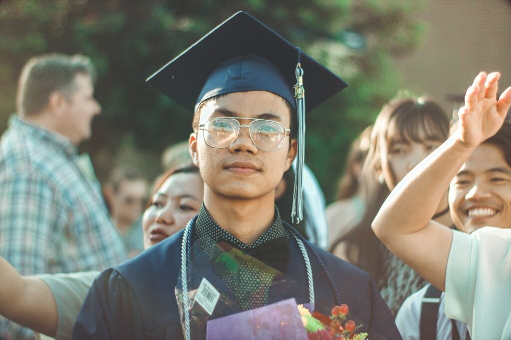 Graduate in cap and gown. Apply economics to your daily life by considering college an opportunity cost.