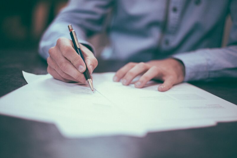 HR professionals and supervisors must be aware of multiple employment laws. Image of papers spread on a desk, focused on a hand holding a pen over the paper.